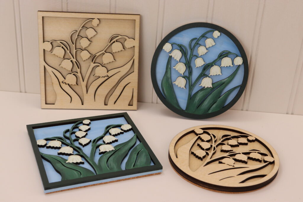 This set of 4 coasters is a mix of unfinished and hand painted in both round and square formats. Each piece is laser cut and layered to give dimension. One square and one round is hand painted with 2 very similar, yet slightly different Lily designs. The flowers are a creamy white with dark green leaves on a sky blue background. The border is dark green finishes the look. The other 2 round and square coasters are the same design as the painted ones, but left unfinished with just a light protective coat of poly to finish them off, allowing the laser cut design to stand out on its own. Each coaster has a layer of cork on the back for grip and insulation.